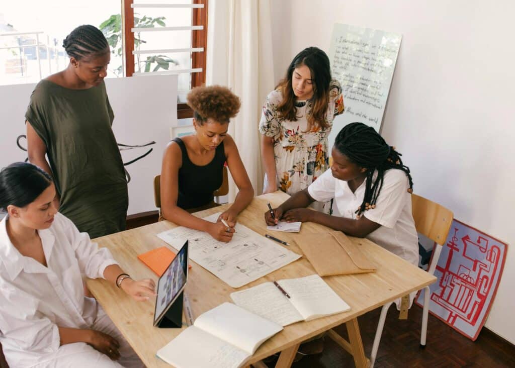 Group of 5 people around a table in a well lit room working together on a document.